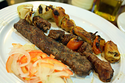 beef and chicken kebab with grilled tomatoes and onions and pickled vegetabbles on a plate